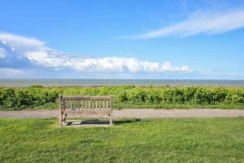 a wooden bench sitting in the grass near a field at Amazing Beachside 2BD Family Home with Garden in Cliftonville