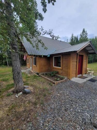 a log cabin with a red door next to a tree at Sterling Cabin close to Kenai River in Sterling