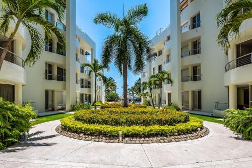 a garden in front of a building with palm trees at Ocean-view condo with resort pool & sundeck in Nuevo Vallarta