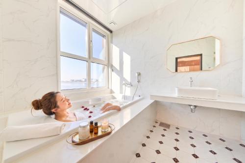 a woman laying in a bath tub in a white bathroom at Restia Incheon Bay Hotel in Incheon