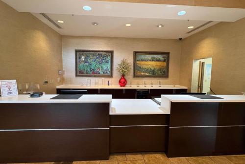 a large kitchen with white counters and paintings on the wall at Hawthorn Extended Stay by Wyndham West Palm Beach Airport in West Palm Beach
