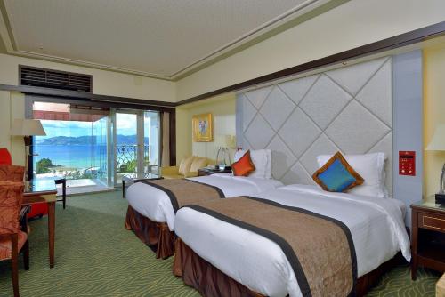 two beds in a hotel room with a view of the ocean at Okinawa Kariyushi Resort EXES Onna in Onna