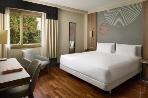 ein Hotelzimmer mit einem großen weißen Bett und einem Schreibtisch in der Unterkunft iStay by NH Zaragoza Sport Hotel in Saragossa