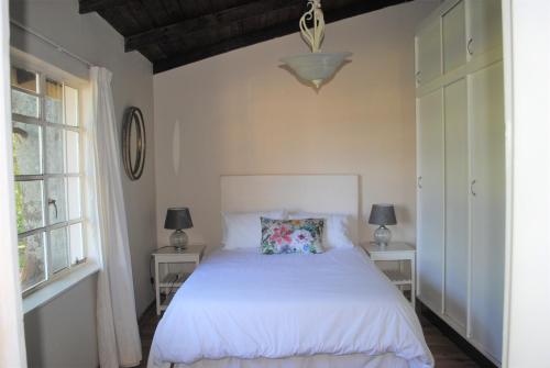 a bedroom with a white bed and two windows at 37 Valley View Cottage in Underberg