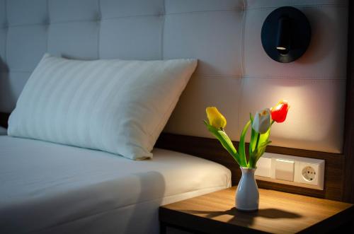 a vase with flowers on a table next to a bed at Hotel Alina in Wiesbaden