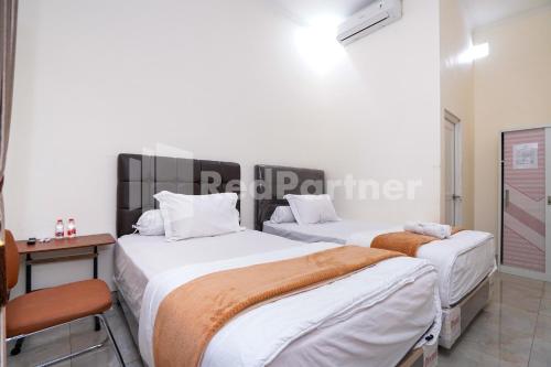 two beds in a room with a table and a desk at Griya Poerwoto Syariah near Pasar Klewer Solo RedPartner in Solo