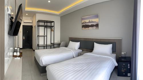 two beds in a hotel room with white sheets at Koa Living Semarang in Kalibanteng-kidul