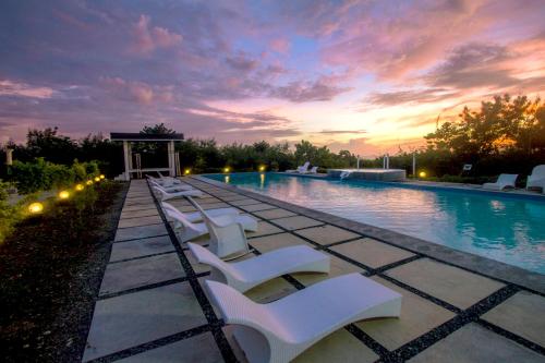 a swimming pool with white chairs and a sunset at Alta Bohol Resort powered by Cocotel in Tagbilaran City
