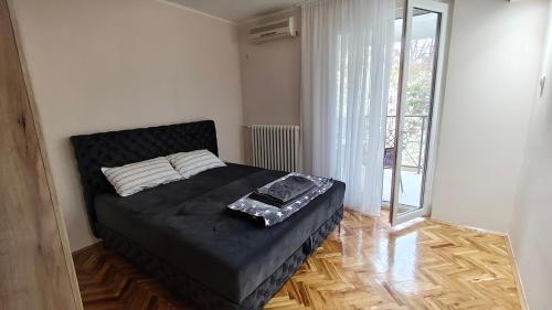a bedroom with a black bed in a room with a window at Green view apartman Pančevo in Pančevo
