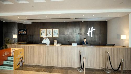 two people sitting at a counter in a hotel lobby at Holiday Inn Abu Dhabi by IHG in Abu Dhabi