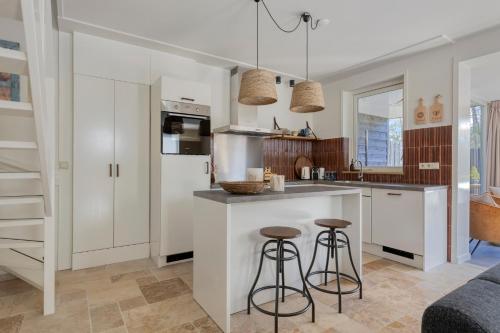 a kitchen with white cabinets and bar stools at Groenendijk Verhuur Vakantiewoning Casa Iris in Burgh Haamstede