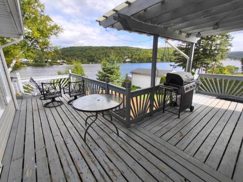 a deck with a grill and a table and chairs at Waterfront with Spa - Etoile Filante in Saint Zenon
