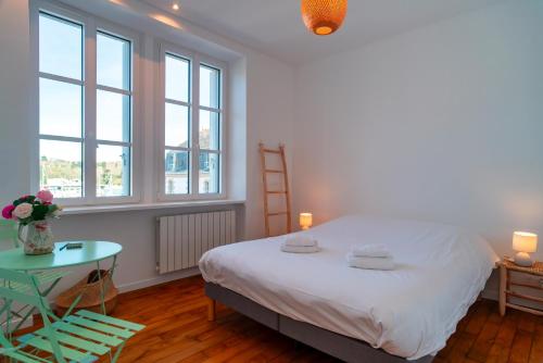 a bedroom with a bed and a table and windows at Lumineux logement vue sur le port in Audierne