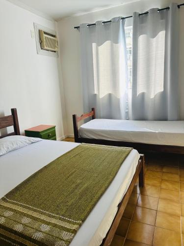 two beds in a room with a window at PRAIA DO MORRO NA QUADRA DO MAR com 2 Quartos sendo 1 Suíte mais Kit Praia e ao lado PRAIA CENTER in Guarapari