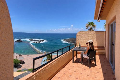 a woman sitting at a table on a balcony looking at the ocean at Terraza con vistas al mar Tenerife Norte Mesa del Mar in Tacoronte