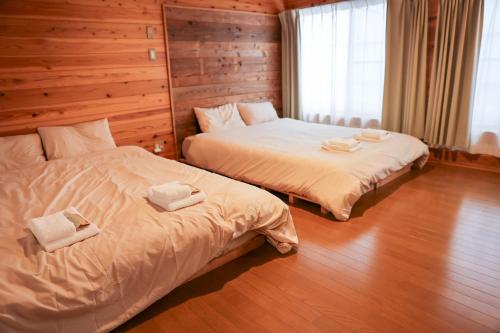 two beds in a room with wooden walls at Aburatsu Inn Kadocco in Nichinan