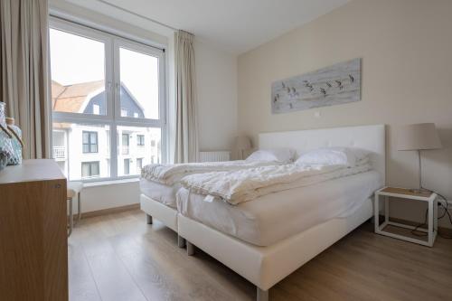 a white bedroom with a bed and a large window at Duinhof IX E204 in Cadzand