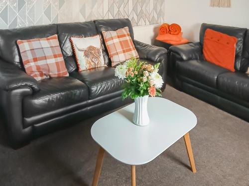 a black leather couch with a vase of flowers on a table at Puffin Cottage in Fraserburgh