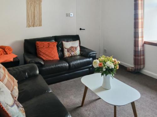 a living room with a black leather couch and a table at Puffin Cottage in Fraserburgh