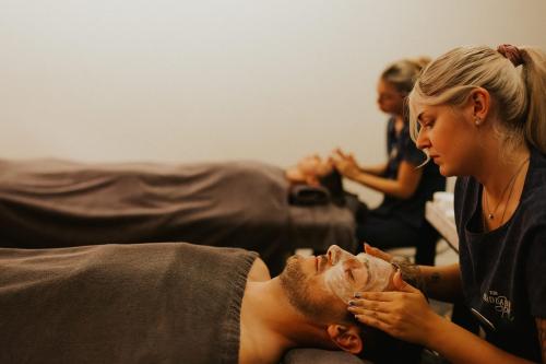 a woman is cutting a mans face while sitting on a couch at The Headland Hotel and Spa in Newquay
