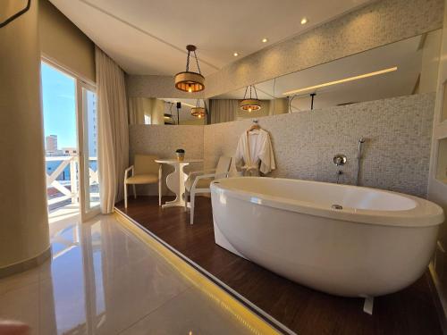 a bathroom with a large white tub and a table at Jatobá Praia Hotel in Aracaju