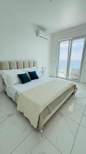a white bedroom with a large bed with blue pillows at Eddy's Luxury Suites - Ilyonis in Shëngjin