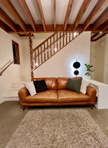 a brown leather couch in a living room with a staircase at Beech Hill - Pet Friendly Holiday Home in Tasman