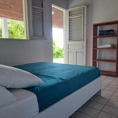 a bedroom with a bed with blue sheets and a window at La Maison Rose in Le Robert