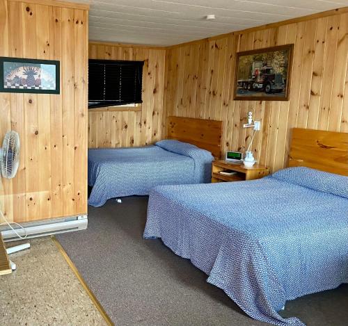 two beds in a room with wooden walls at Chicken Shack Motel in Batchawana