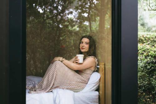 a woman sitting on a bed holding a cup of coffee at Pinelight Retreat in Kuei-chu-lin