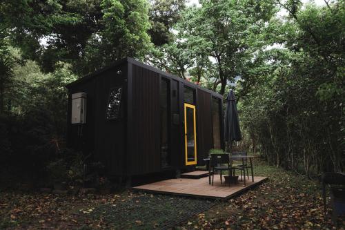a black tiny house with a table and an umbrella at Pinelight Retreat in Kuei-chu-lin