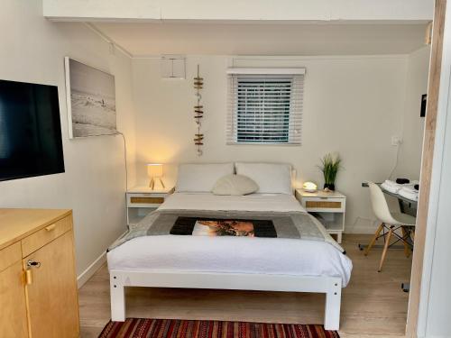 a white bedroom with a bed and a television at Turtle Cabin in Papamoa
