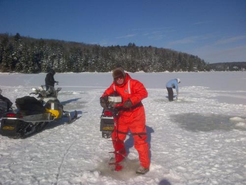 a man standing in the snow next to a snowmobile at Little Hawk Resort & Marina in Algonquin Highlands