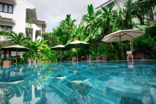 a large swimming pool with umbrellas in front of a building at East West Villa in Hoi An