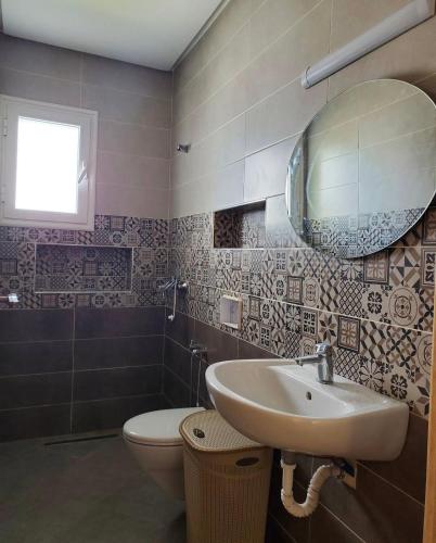 a bathroom with a sink and a toilet and a mirror at Résidence Nafissa Ezzahra Kelibia in Ḩammām al Ghazzāz