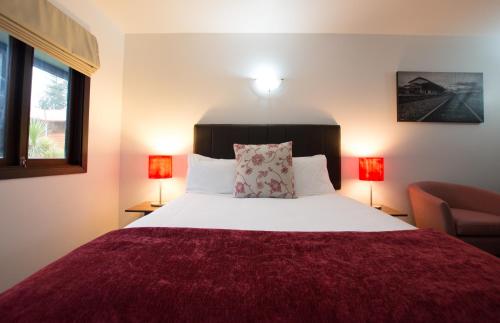 a bedroom with a bed with a red blanket and two lamps at The Park Hotel Ruapehu in National Park