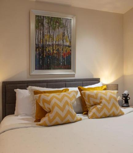 a bed with yellow and white pillows and a painting on the wall at Westminster 1 bed apt with terrace and Air-Con in London