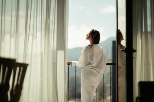 a woman in a robe looking out of a window at Wulfenia Hotel & Spa in Kolašin