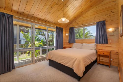 a bedroom with a bed and large windows at Sea Breezes in Matarangi