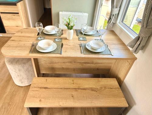 a wooden table with plates and wine glasses on it at Shamrocks Cove Caravan - Award-Winning Coastal Retreat in Crantock