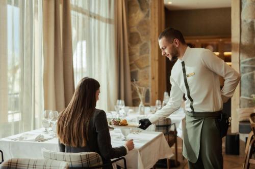 a man serving a woman a plate of food in a restaurant at Wulfenia Hotel & Spa in Kolašin