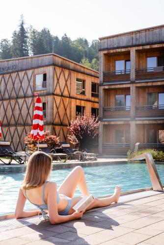 a woman reading a book next to a swimming pool at Tirol Lodge in Ellmau