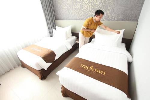 a man making a bed in a hotel room at Midtown Hotel Samarinda in Samarinda