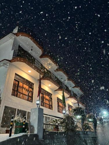 a building at night with snow falling in front of it at Hotel Sumit in Kausani