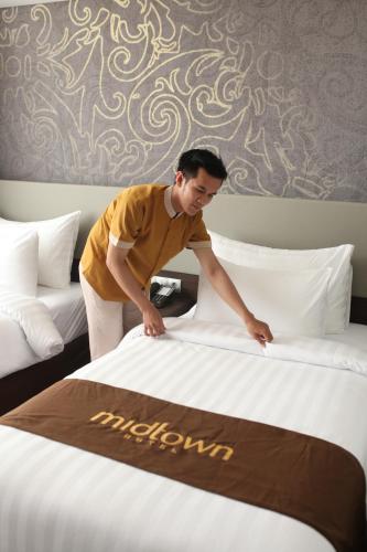 a man making a bed in a hotel room at Midtown Hotel Samarinda in Samarinda