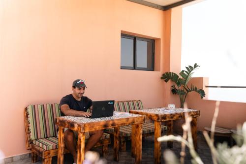 a man sitting at a table with a laptop at Tasga Guest House in Tamraght Ou Fella