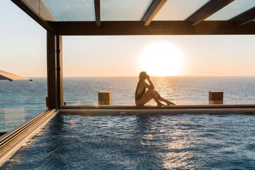 a woman sitting on the edge of a swimming pool overlooking the ocean at Bellevue On The Beach Suites in Rhodes Town