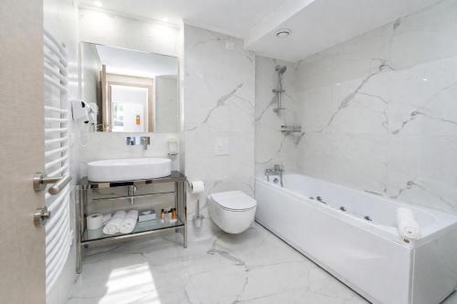 a white bathroom with a tub and a toilet and a sink at Hotel Alexandar II in Skopje