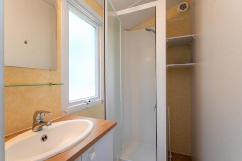 a bathroom with a sink and a shower with a window at Mobil home 2 Bikini in Plouha