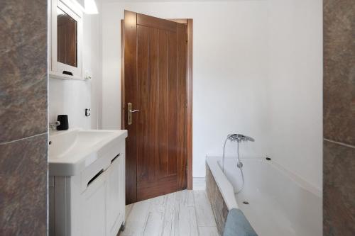 a bathroom with a wooden door and a tub and a sink at Breathe Nature - Beach House Azores in Feteira